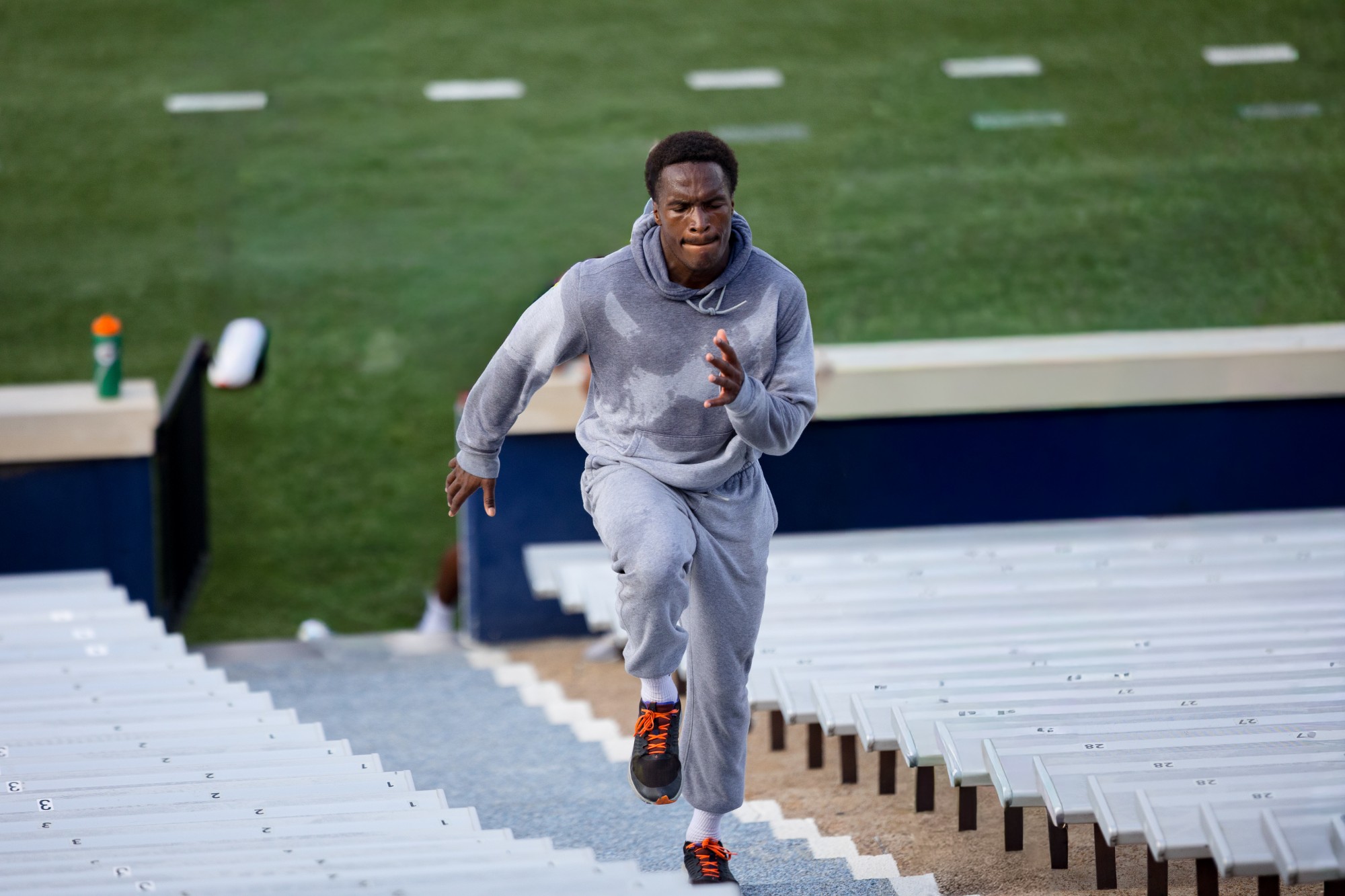 Lawrence running stadium stairs in a sweat-soaked hoodie